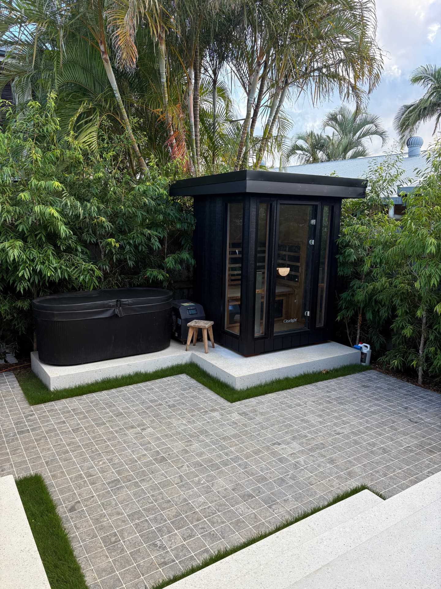 Black sauna and plunge tub on travertine paving with palms behind